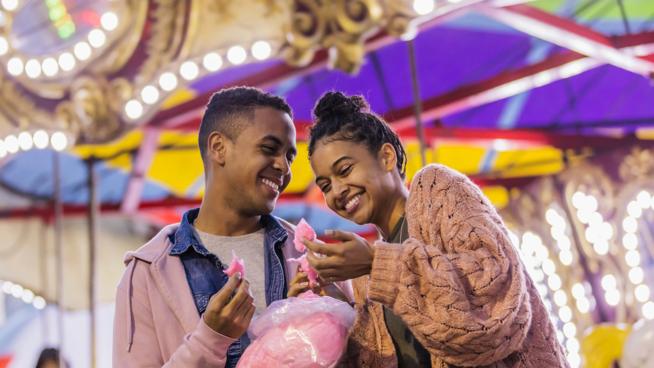 Couple eating cotton candy in front of carousel ride