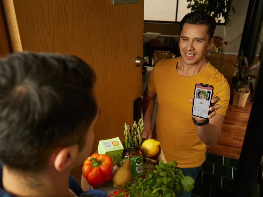 A man receiving fruits and vegetables on your door with a cell phone on your hands 