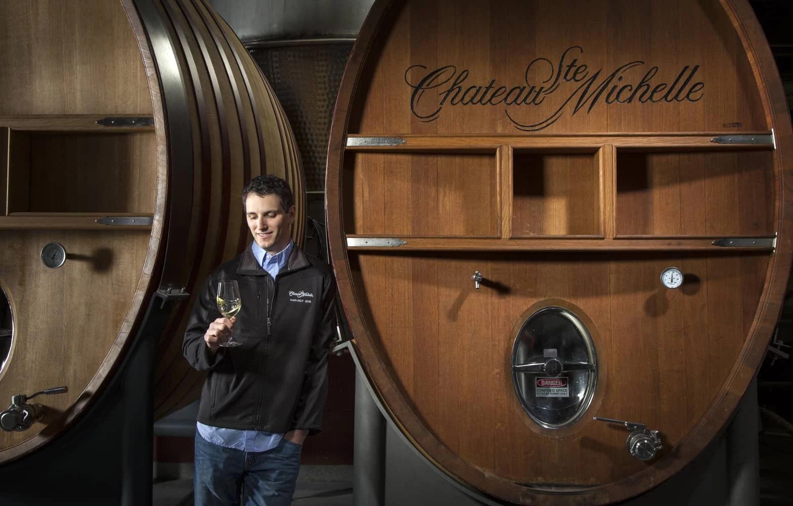 Man looking at a glass on wine in front of a wine barrel
