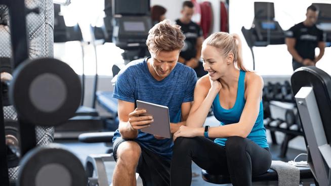 Zwei Personen in einem Fitnessstudio schauen gemeinsam auf ein Tablet
